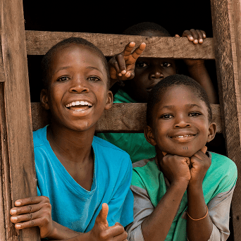 Children giving a thumbs-up through a wooden window frame at a charity outreach