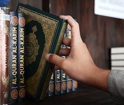 Hands holding a Qur'an prepared for distribution to students and mosques
